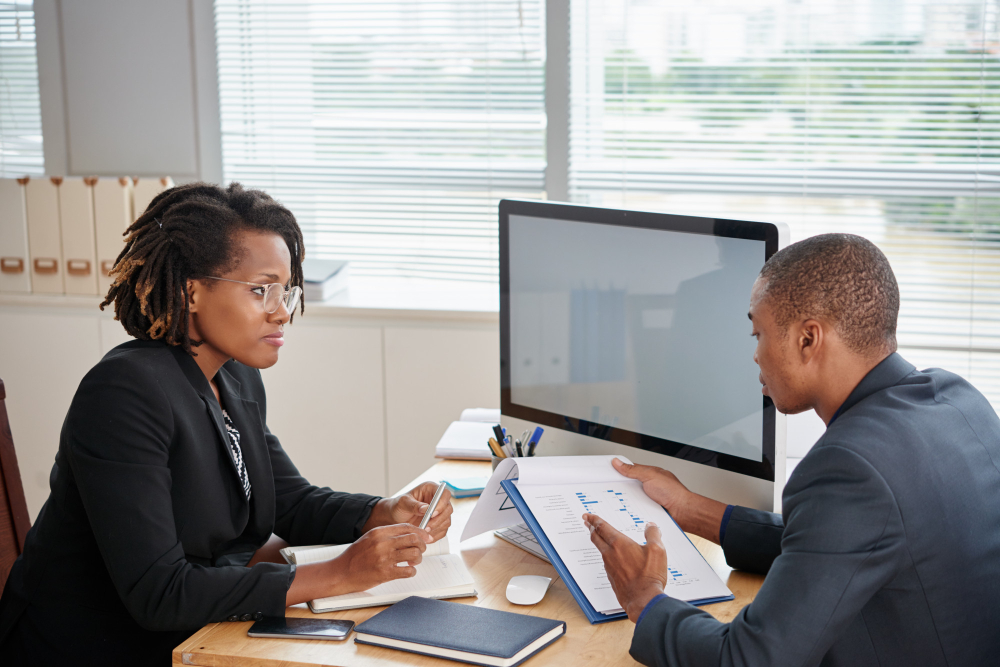 Afro-American man in suit holding documents and talking to female boss showing courtesy